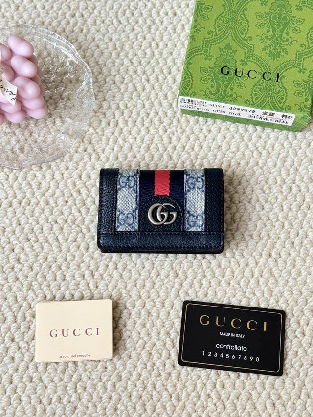 Gucci 折叠卡片夹，配以醒目的标志性双 G 金属配件。采用帆布配织带制作，以营造织纹外观。 型号：428737 尺寸：10.5×7.5×2.5